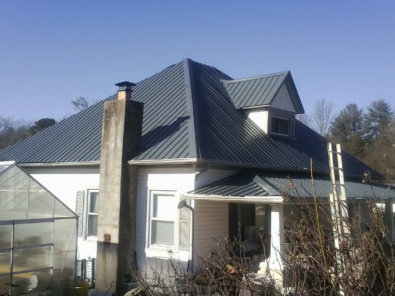 Dark blue standing seam metal roof on a white farmhouse with dormer — Slate & Tile Roof Repair by Roofing Brothers in Saxton