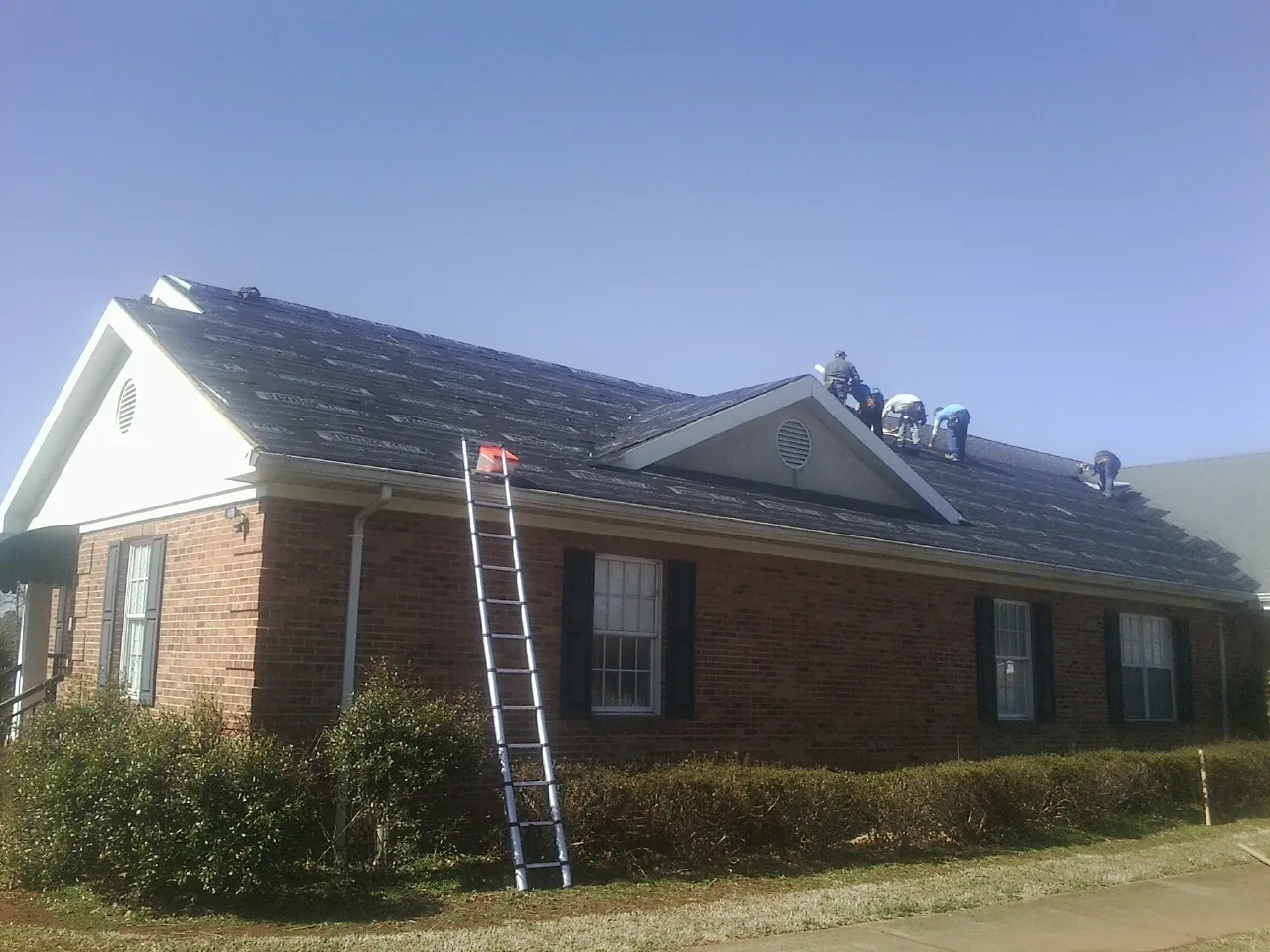 Crew tearing shingles off a brick ranch roof with a ladder set — Metal Roof Repair work by our crew in Saxton