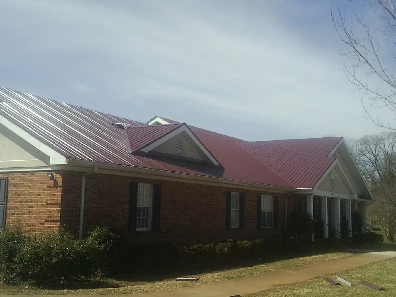 Red metal roof with gabled entries on a long brick building, from a Hail Damage Roof Repair job in Saxton