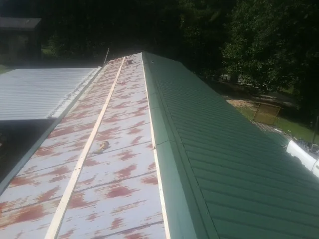 Old rusted panels beside newly installed green metal roofing — Wind Damage Roof Repair by Roofing Brothers in Saxton