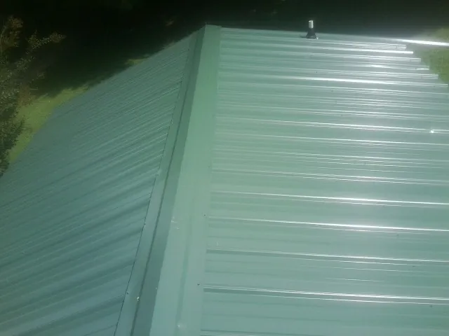 New green metal panels meeting at the ridge of a roof — Flat Roof Repair work by our crew in Saxton