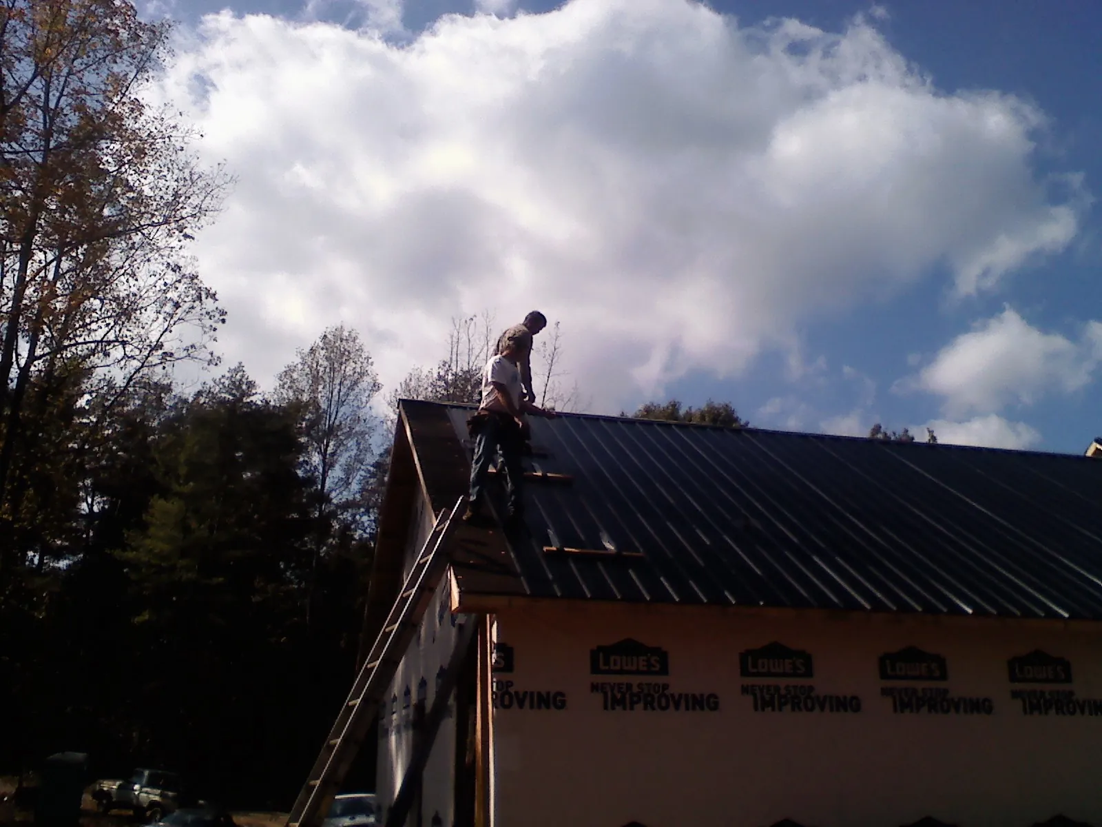 Roofer fastening dark metal panels high against a cloudy sky, from a Roof Inspection job in Saxton