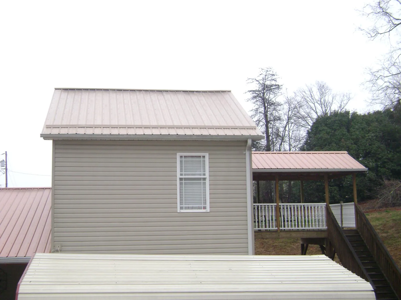 Tan metal roofs on a two story addition and attached porch, from a Roof Replacement job in Saxton